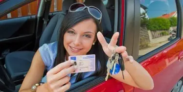 Smiling woman holding a German driver’s license inside a red car